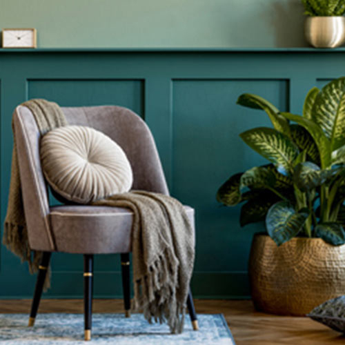 Cozy upholstered armchair with round cushion stands in a room with a houseplant and other decorative elements.